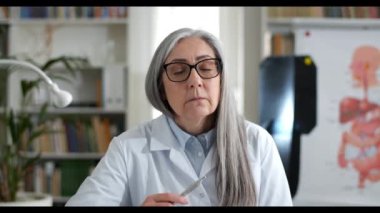 Gözlüklü kadın doktorun görüntüsü. Hasta dinliyor ve video konsültasyonu yaparken başını sallıyor. Rob 'da bir kadın konuşuyor ve tıbbi ofiste kameraya bakıyor. Teletıp.