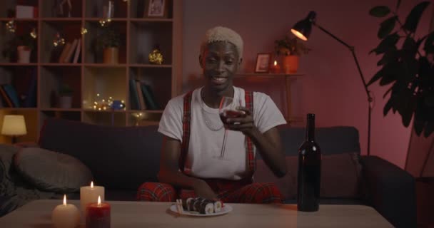 Excited man cheering with wineglass and drinking while having online conversation. Afro american guy smiling and talking while looking to camera and sitting at home. Concept of online date. — Stock Video
