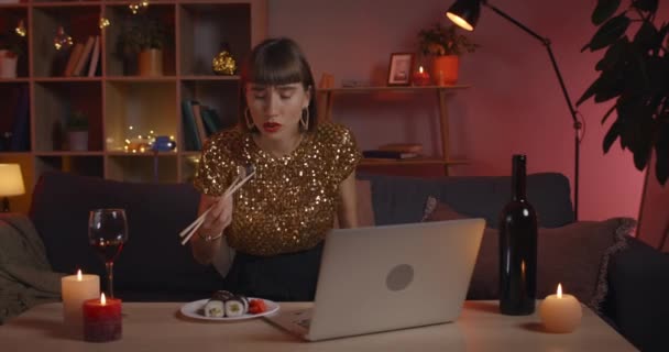 Millennial femme manger des rouleaux de sushi savoureux tout en ayant appel vidéo en ligne. Personne féminine attrayante souriant et parlant tout en regardant l'écran d'ordinateur portable. Concept de communication. — Video