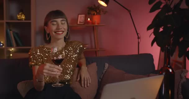 Vista Crop di bella donna ridendo e bevendo vino da vetro mentre guardando lo schermo del computer portatile. Gioiosa persona femminile in abiti eleganti che comunica online mentre è seduta sul divano. — Video Stock