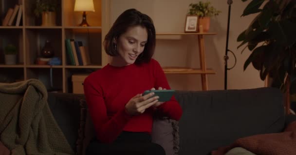 Widok na zboże młodej kobiety oglądającej wideo i dotykającej ekranu telefonu siedząc na kanapie w domu. Wesoły kobieta osoba za pomocą trzymając smartfona poziomo.. — Wideo stockowe