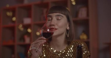 Şarap kadehinden içen neşeli kadın internette konuşurken gülümsüyor. Kameraya bakıp evde otururken gülen neşeli bir kadın. Çevrimiçi tarih kavramı.