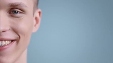 Genç ve neşeli bir adamın yüzünün yarısı mesaj atmak için boş yere kameraya bakarken. Stüdyo arka planında poz verirken gülümseyen açık mavi gözlü erkek portresi.