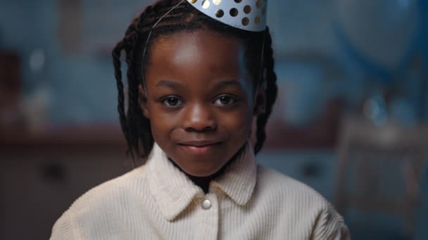 Portret małego afro amerykańskiego chłopca uśmiechającego się i patrzącego do kamery. Portret uroczego wesołego dziecka w kapeluszu urodzinowym radującego się podczas pozowania. Dziecko urodzinowe. — Wideo stockowe