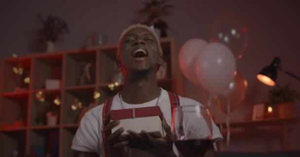 Excited afro american man in birthday hat looking to camera and laughing .Handsome male person rejoicing and saying wow while opening present box and having online conversation at home. — Stock Video