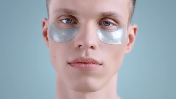 Crop view of young man with hydropeptide patches opening eyes and smiling while looking to camera . Portrait of male handsome model with light blue eyes posing. Concept of skincare. — Stock Video