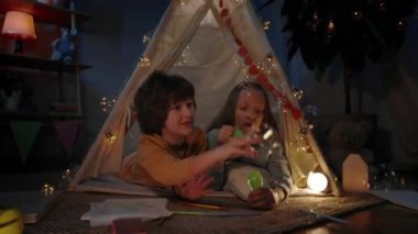 Dekoratif derme çatma çadırdaki çocuklar akşamları evlerinde baloncukları üflüyorlar. Neşeli kız ve oğlan iyi vakit geçirirken yerde yatıyorlar. Boş zaman ve dikkatsiz çocukluk kavramı.