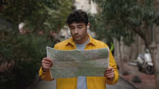 一个戴耳机的帅哥拿着地图在街上走着 — 图库视频影像