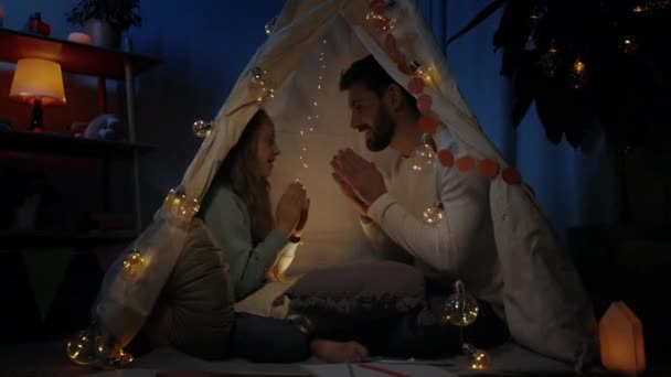 즐거운 아버지와 그 의 십 대 소녀는 임시 오두막에 앉아 함께 즐거운 시간을 보내며 놀이를 하고 있다. 행복 한 가족 시간에 대한 개념. — 비디오