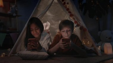 Gençler akşamları evlerinde dekoratif derme çatma kulübelerde internete göz atarken vakit geçiriyorlar. Kız ve oğlan akıllı telefonlar kullanırken yerde yatıyorlar. Boş zaman kavramı..