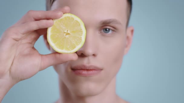 Снимок красивого мужчины с половиной лимона, смотрящего в камеру. Мужчина молодая модель с светло-голубыми глазами позирует с фруктами.. — стоковое видео