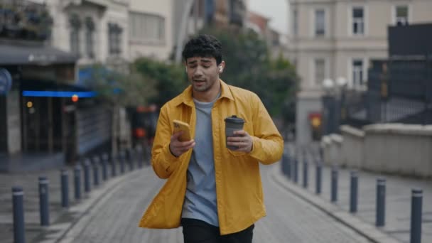 Joyful guy in earphones walking and singing on city street — Stock Video
