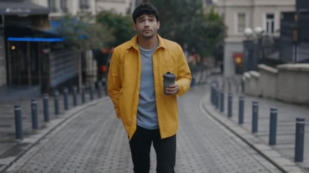 Стильний чоловік, що йде з чашкою кави на міській вулиці — стокове відео
