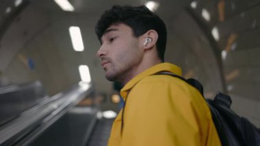 Sırt çantalı bir erkek yolcu yürüyen merdivende ilerliyor.