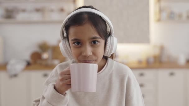 Позитивная индианка в наушниках пьет чай на кухне — стоковое видео