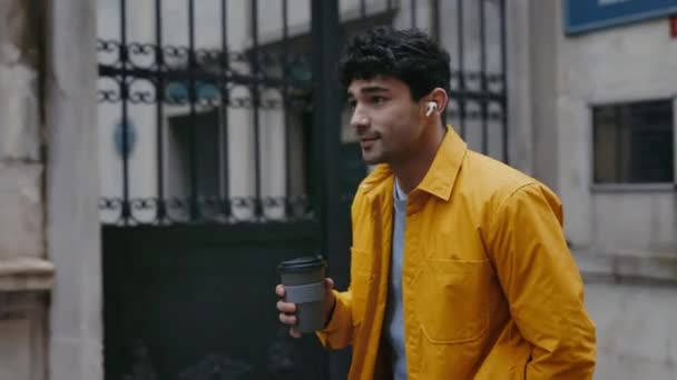 快乐的男人戴着耳机走在街上，喝着咖啡 — 图库视频影像