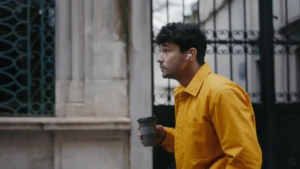 आदमी इयरफ़ोन में संगीत सुन रहा है और शहर में कॉफी पी रहा है — स्टॉक वीडियो