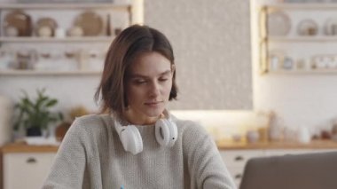 Öğrenci masada dizüstü bilgisayarla otururken kameraya bakıyor