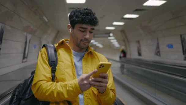 Hombre sonriente en chaqueta amarilla usando móvil en escaleras mecánicas — Vídeo de stock