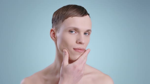 Portretul unui bărbat atrăgător atingând fața cu o mână în timp ce se uită la cameră. Portret de model masculin cu ochi albaștri deschiși pozând. Conceptul de cosmetologie, îngrijire a pielii . — Videoclip de stoc