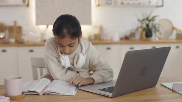 Focused muslim child reading book and typing on laptop — Stock Video