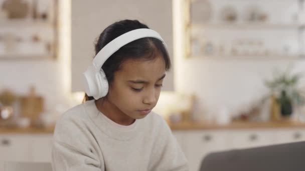 Девочка-подросток в наушниках, печатающая на современном ноутбуке — стоковое видео