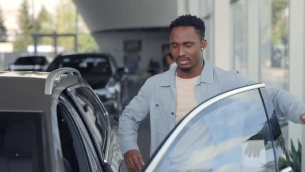 Улыбающийся африканский мужчина покупает новую машину в автосалоне — стоковое видео