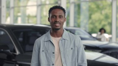 Gülümseyen Afrikalı adam modern araba galerisinde duruyor.
