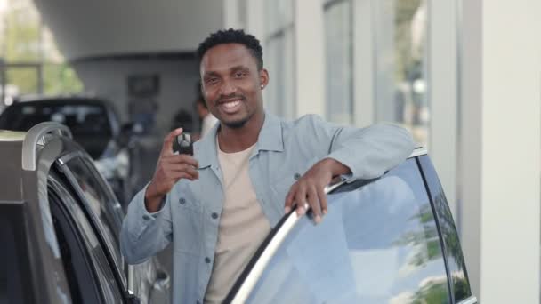 Sonriente hombre africano posando cerca del coche con llaves en las manos — Vídeos de Stock