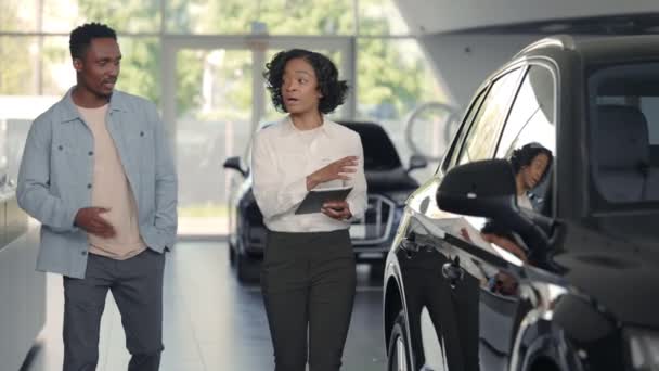 Verkäuferin mit Tablet zeigt Kunden im Salon Autos — Stockvideo