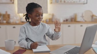 Video dersi sırasında gülümseyen ve el sallayan Afrikalı bir öğrenci.