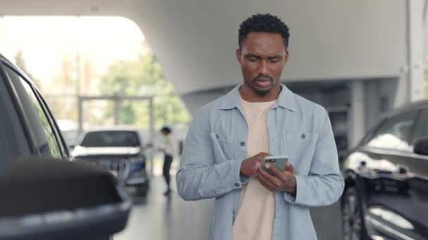 Hombre africano utilizando el móvil para comprobar los detalles sobre el coche nuevo — Vídeo de stock