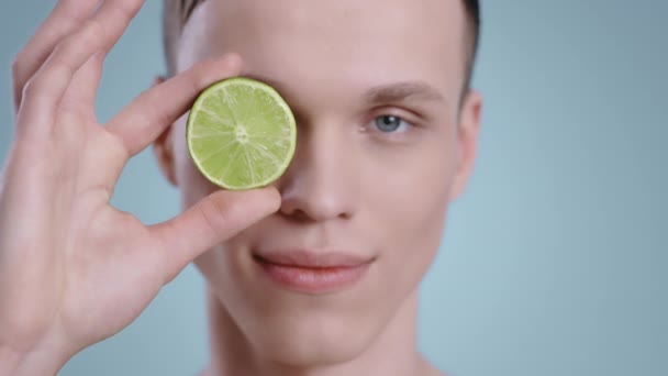 Huvudskott av stilig man som håller hälften av lime medan du tittar på kameran. Manlig ung modell med ljusblå ögon poserar med frukt .Begreppet hudvård, sjukvård. — Stockvideo