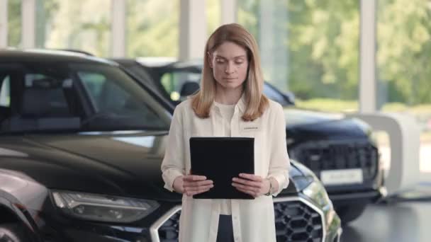 Attraktive Frau mit Klemmbrett posiert bei modernem Autohaus — Stockvideo