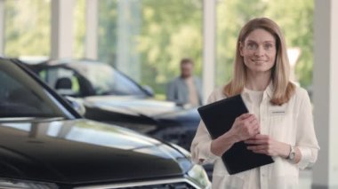 Otomobil kuaförü elinde pano, kamerada gülümsüyor.