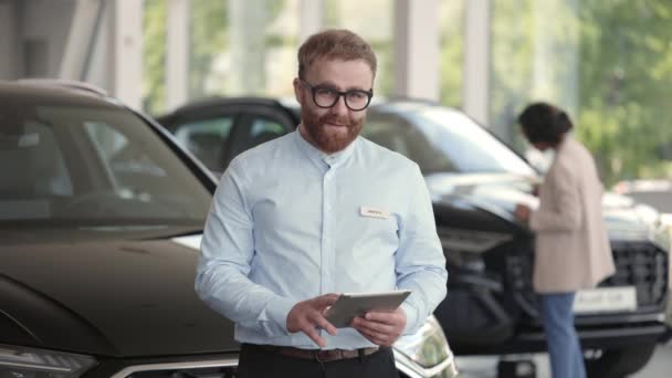 Retrato del distribuidor masculino posando en el salón de automóviles con la tableta — Vídeos de Stock