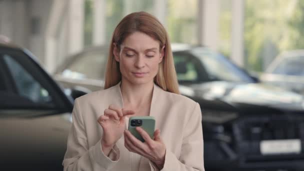 Mujer feliz usando teléfono inteligente al comprar un coche en la concesionaria — Vídeos de Stock