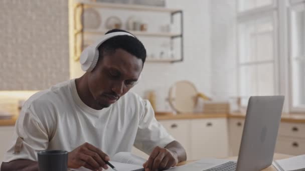 Evde ders çalışmak için bilgisayar ve kulaklık kullanan Afrikalı bir adam. — Stok video
