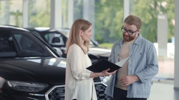 Frau hält Klemmbrett, während Mann im Autosalon signiert — Stockvideo