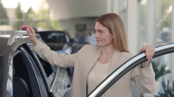 Charmante Frau steht neben Luxusauto in modernem Autohaus — Stockvideo