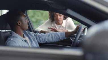 Afrikalı bir kadın galeride erkek müşteriye araba gösteriyor.