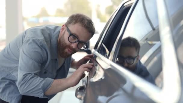 Szczęśliwy człowiek w okularach dotykający samochodu w nowoczesnym salonie — Wideo stockowe