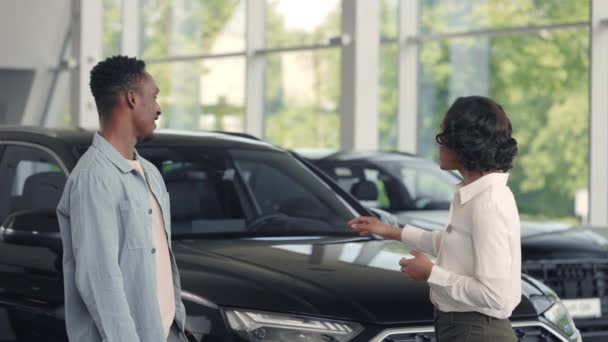 Hombre africano de pie con concesionario de coches en la sala de exposición — Vídeos de Stock