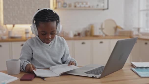 Menina Africano livro de leitura enquanto sentado à mesa com laptop — Vídeo de Stock