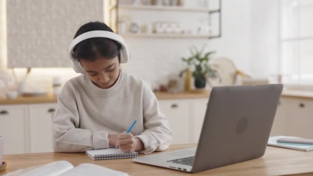 Menina indiana escrevendo em copybook durante a aula on-line em casa — Vídeo de Stock