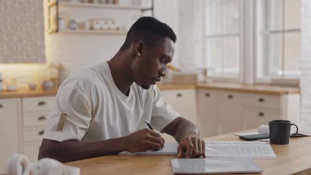 Estudiante haciendo sinopsis mientras lee libro en la mesa de la cocina — Vídeos de Stock