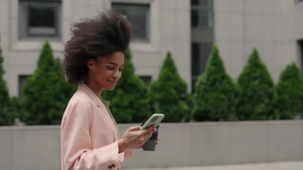 Gelukkig jong gemengd ras zakenvrouw met behulp van haar smartphone tijdens het lopen en dansen op straat. Stadstechnologie en dansen bij het muziekconcept — Stockvideo