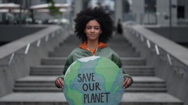 Gezegenimizi kurtarın. Durgun, çok kültürlü kızın belden aşağı portre görüntüsü. Sokakta duruyor ve kameraya gösterirken dünyanın şeklini tutuyor..