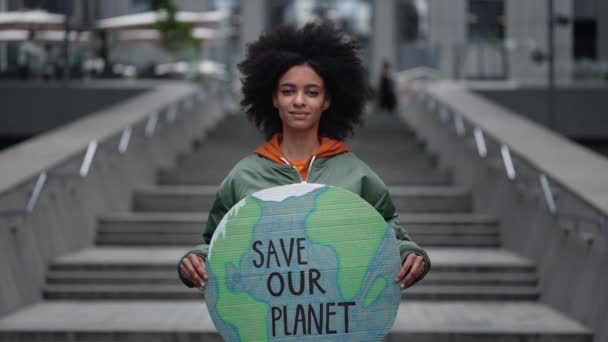 Uratować naszą planetę. Pas w górę widok portret spokojnej wielorasowej dziewczyny stojącej na ulicy i trzymając sztandar w kształcie ziemi, pokazując go do kamery. — Wideo stockowe
