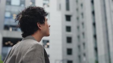 Yeni bir iş. Rüzgâr saçlarını savururken esmer beyaz iş adamının iş merkezine bakışı. Meslek ve insan yaşam tarzı kavramı.